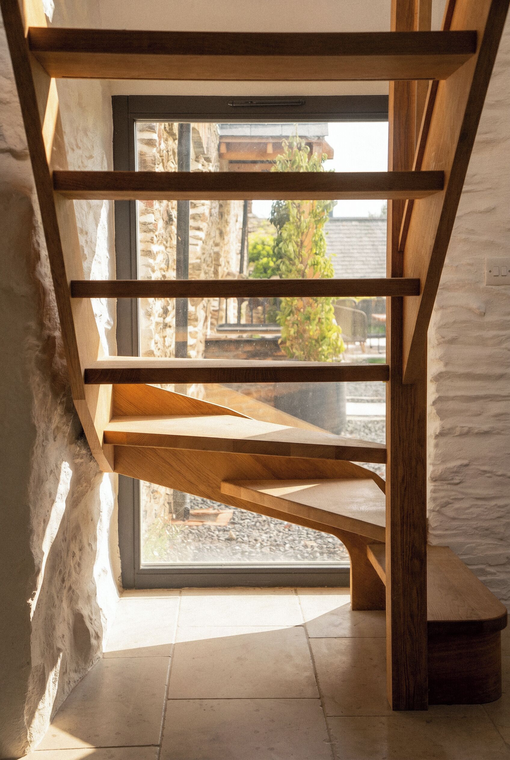 A wooden staircase with a curved design, leading to a window overlooking an outdoor area.