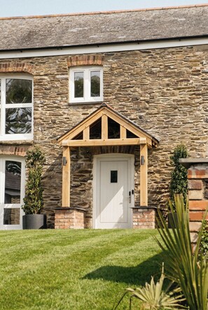 A stone building with a white door, wooden porch, and potted plants.