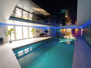Ein modernes Hallenbad mit freiem Blick auf den Poolbereich, einer Decke mit Sternenprojektion und einer Tür zu einem anderen Raum.