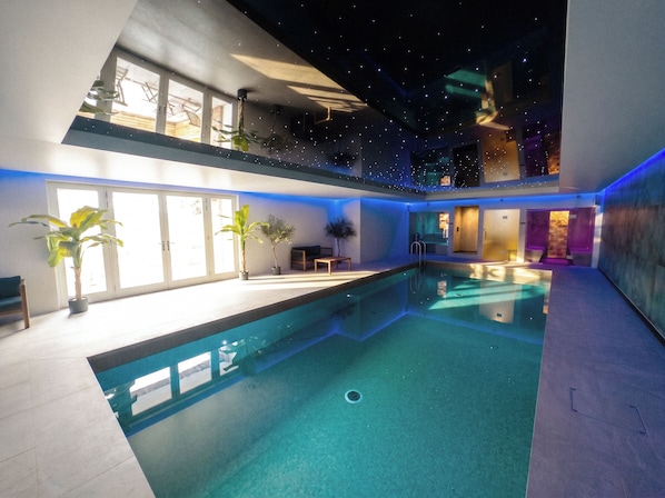 A modern indoor swimming pool with a clear view of the pool area, a ceiling with a star projection, and a door leading to another room.