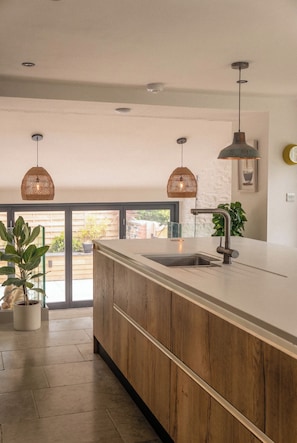 A modern kitchen with a large island, pendant lighting, and a view to the outside.