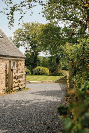 A stone building with a gravel driveway leading to a wooden gate.