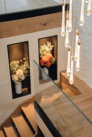 Un escalier avec des rampes en verre, des marches en bois et deux compositions florales dans des vases blancs.