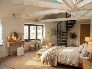 Ein Schlafzimmer mit Bett, Stuhl, Schreibtisch, Spiegel, Fenster und einer Wendeltreppe.