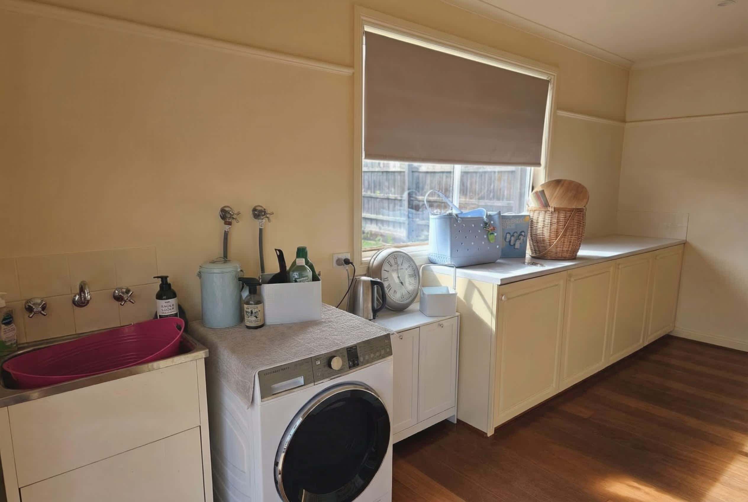 A compact laundry room with a washing machine, a sink, and a window with a blind.
