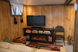 A cozy living room with a television, board games, a fireplace, and a comfortable couch.