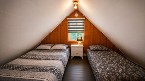A small, cozy attic bedroom with two beds, a nightstand, and a window with blinds.