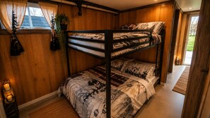 Une chambre avec un lit superposé, un mur en bois, une fenêtre avec des rideaux, une plante en pot et une table de chevet avec des bougies.
