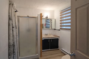Ein Badezimmer mit Dusche, Waschbecken, Spiegel und einem Fenster mit Jalousien.