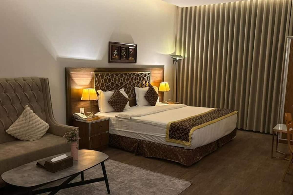 A hotel room with a bed, a sofa, a coffee table, a nightstand, and a lamp.