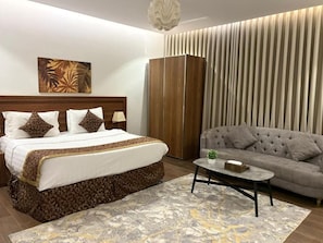 A hotel room with a bed, a sofa, a coffee table, a wardrobe, and a painting on the wall. - سوار الذهب للشقق المخدومه (Madinah)