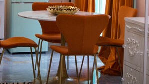 En matplats med ett gammalt, turkosfärgat kylskåp, orange stolar, ett bord i marmor och ett fönster med orange gardiner.