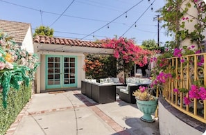 A patio with outdoor furniture, a small building with a green door, and flowering plants.