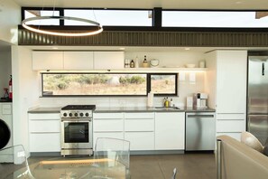 Une cuisine moderne dotée d’une grande fenêtre, d’appareils électroménagers en acier inoxydable et d’une table à manger en verre.