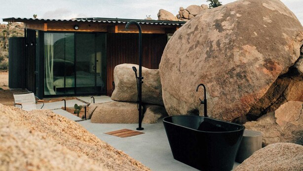 A modern building with a glass facade, large rocks, and a black bathtub. - Rock Cove By Homestead Modern (Pioneertown)