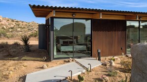 A modern building with large glass windows, a wooden roof, and a desert landscape. - Rock Cove By Homestead Modern (Pioneertown)