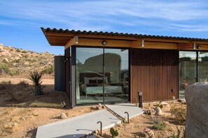 Un bâtiment moderne doté de grandes fenêtres en verre, d’un toit en bois et surplombant un paysage désertique.