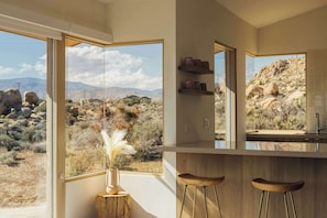 Eine Küche mit einem großen Fenster, Holzhockern und Blick auf eine Wüstenlandschaft.