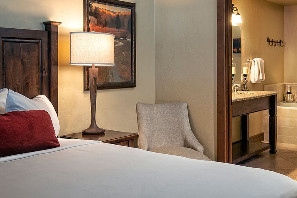 Een hotelkamer met een bed, een stoel, een nachtkastje, een lamp, een schilderij en een badkamer met een wastafel en spiegel.