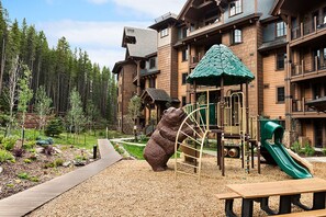 Eine Lodge mit Spielbereich, darunter eine Rutsche und Klettergerüste, umgeben von einem Wald.