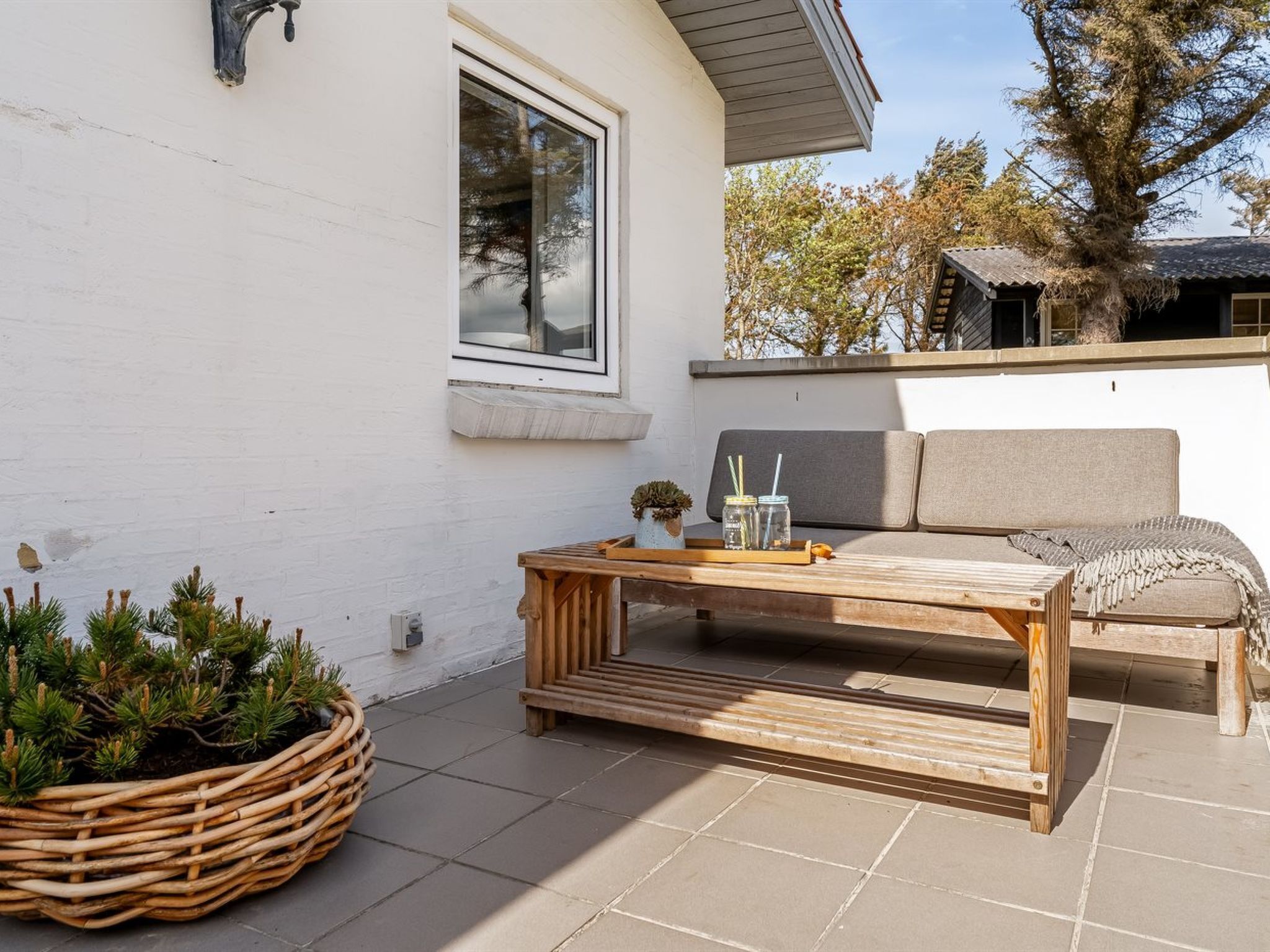 Une terrasse avec une table en bois, un pot de fleurs en osier et un canapé.