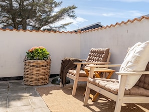 Eine Terrasse mit einem Korbwannenmöbel, zwei Holzstühlen und einem Kissen.