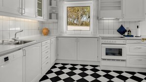 A modern kitchen with white cabinetry, a black and white checkered floor, and a window with a view of trees. - "Senija" - 175m from the sea by Interhome (Blokhus)