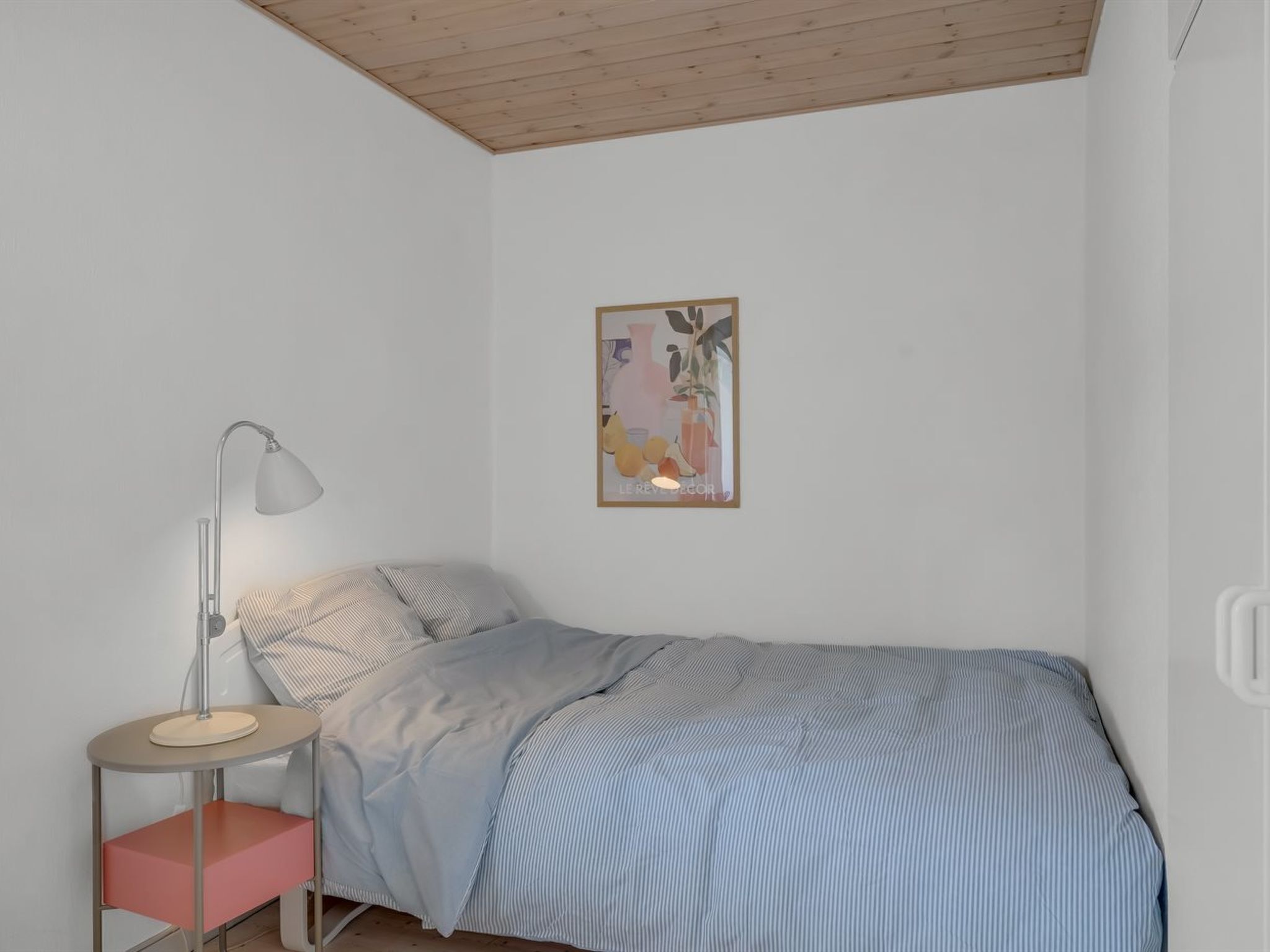 A bedroom with a bed, a bedside table with a lamp, a chair, and a wall-mounted picture.