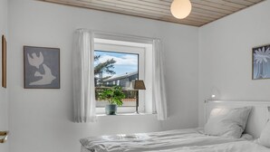 A bedroom with a bed, a window with curtains, a potted plant, and a lamp. - "Senija" - 175m from the sea by Interhome (Blokhus)