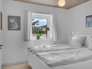 Ein Schlafzimmer mit Bett, einem Fenster mit Vorhängen, einer Zimmerpflanze und einer Lampe.