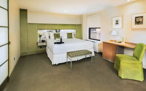 Ein Hotelzimmer mit Bett, Nachttisch, Lampe, Stuhl und Schreibtisch mit Computer.