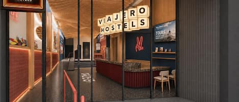 A modern hotel entrance with a visible reception desk, a staircase leading to the upper floor, and a sign indicating the hotel's name.