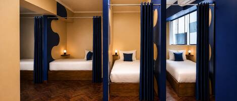 A hotel room with two beds, wooden flooring, and blue curtains.