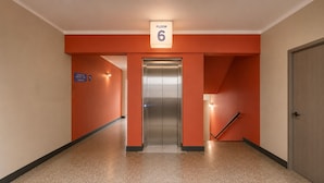 A hotel corridor with a lift, a sign indicating room 6, and a staircase with a handrail. - Viajero Lima - Miraflores Hostel (Lima)