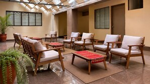 A sunlit indoor seating area with wooden chairs and tables, large windows, and a potted plant. - Viajero Lima - Miraflores Hostel (Lima)