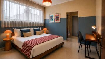 A hotel room with a bed, bedside lamps, a desk with a chair, and artwork on the wall.