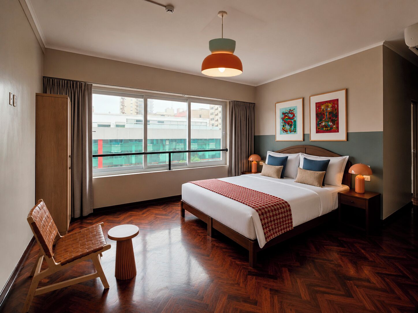 A hotel room with a large bed, a wooden chair, a small table, and a view of the city through large windows.