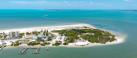 An aerial view of a coastal resort with a marina, beachfront, and dense vegetation.