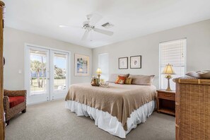 A bedroom with a bed, a ceiling fan, a nightstand, a lamp, and a wicker side table. - Beachside Bliss with Paddleboards, Bikes & Island Fun - Mystic Mandalay - Roelens (Fort Myers Beach)