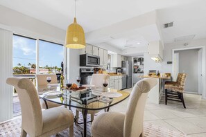 A modern kitchen with a dining area, large windows, and a view of the outdoors. - Beachside Bliss with Paddleboards, Bikes & Island Fun - Mystic Mandalay - Roelens (Fort Myers Beach)
