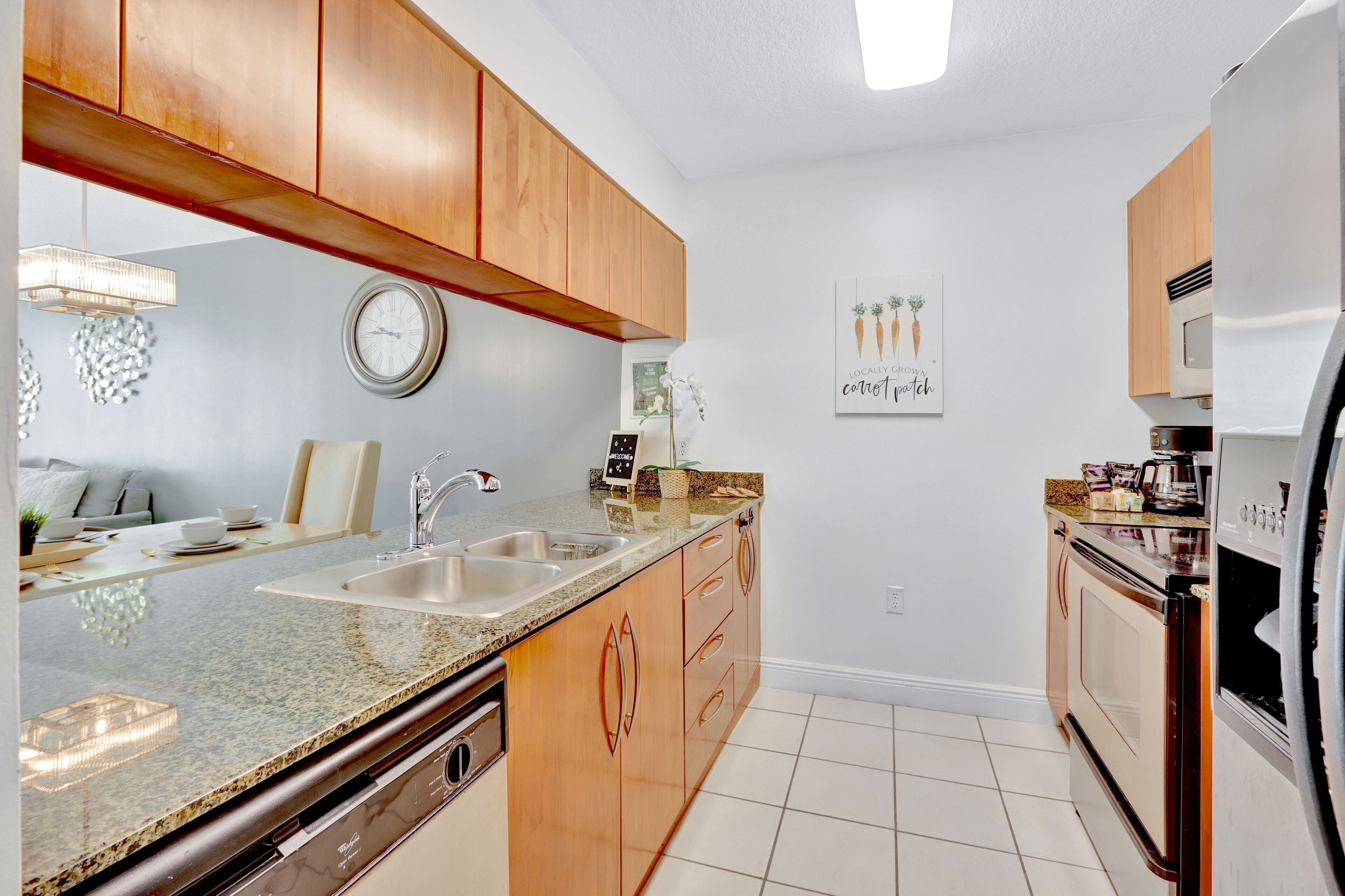 A kitchen with wooden cabinets, a granite countertop, a sink, a clock, and a microwave.