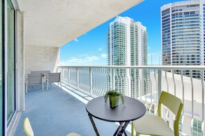 A balcony with a table and chairs, a potted plant, and a view of tall buildings. - The Brickell Estates (Miami)
