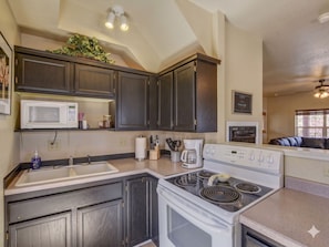 A kitchen with dark cabinets, a microwave, a stove, and a coffee maker. - Union Street Townhouse 2BD/1.5BA Near Whiskey Row (Prescott)