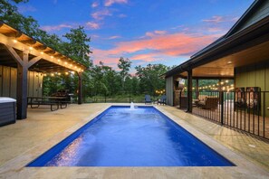 A swimming pool with a fountain, surrounded by outdoor seating and a covered area with string lights.