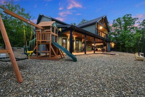 A house with a play area, including a slide and swings, and a covered patio.
