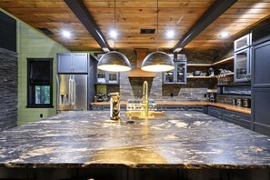 Une cuisine moderne dotée d’un grand îlot central, d’appareils électroménagers en acier inoxydable et d’un plafond au style rustique.