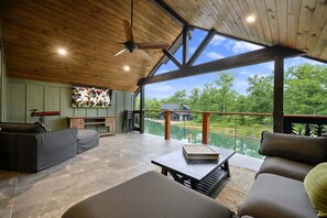 A spacious room with a wooden ceiling, a large window overlooking a green landscape, a fireplace, and a seating area with a table.