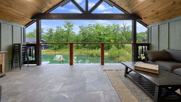 A covered patio with a view of a river, stone flooring, a wooden ceiling, and a sofa.