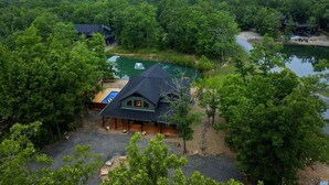 A lodge with a swimming pool, surrounded by dense forest and a lake.