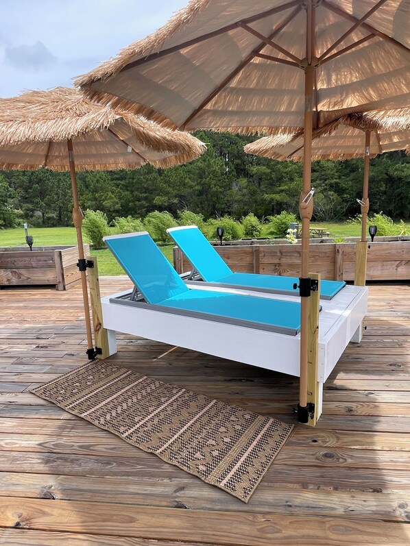 A wooden deck with a pool table, two lounge chairs, and thatched umbrellas.